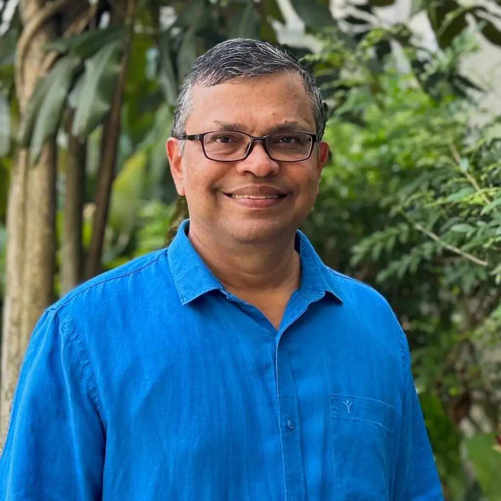 Smiling man in blue shirt with greenery background